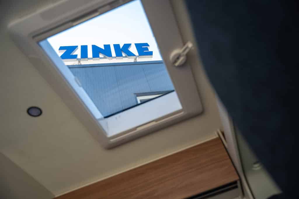 Blick durch das geöffnete Dachfenster eines Wohnmobils auf den Zinke-Schriftzug an der Halle